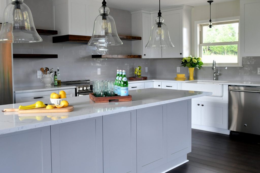 A bright kitchen with a grey island under three glass pendants, lemons on a board and a window over the sink