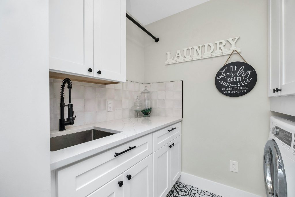 A white laundry room with a deep sink and a front-loading machine beside it