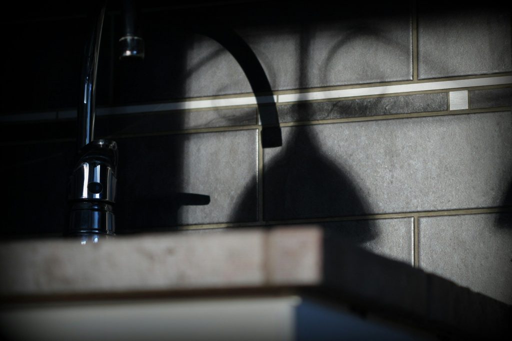 A tap and its shadow across a tiled wall in low light