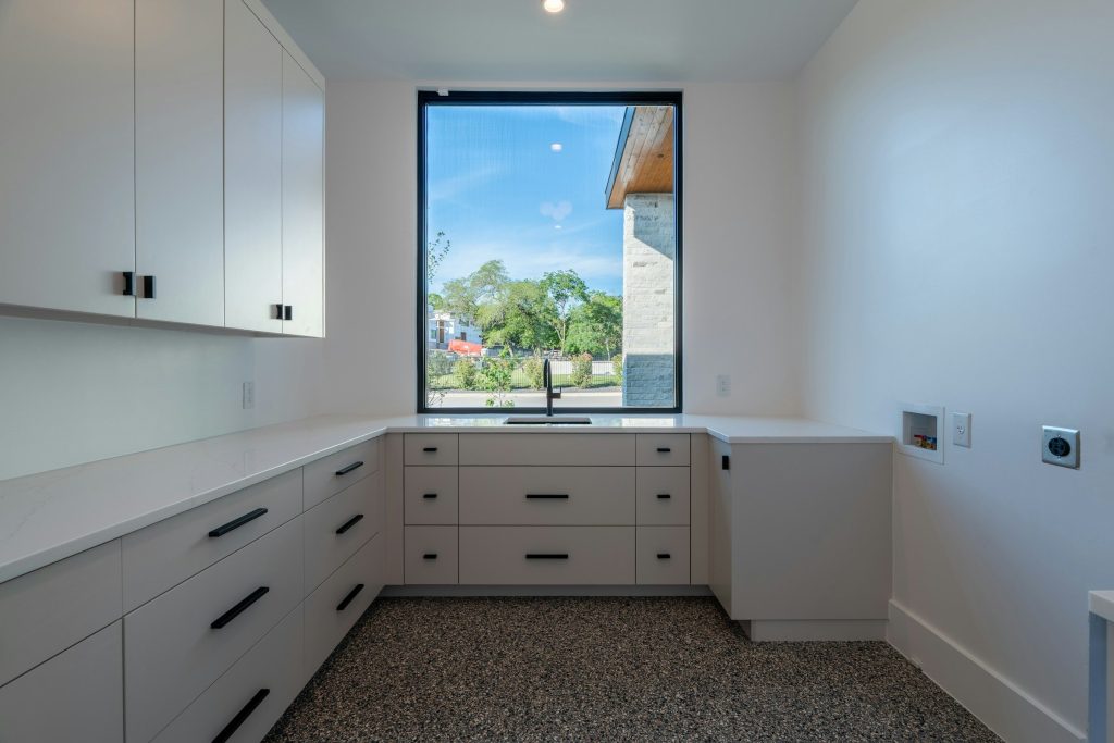 An empty utility room with cabinets, a sink and the outlets for a washer